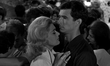 Movie still from “Phaedra” (1962), directed by Jules Dassin – A man and a woman standing next to each other in a crowd; Close Up shot, Low angle