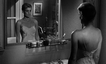 Movie still from “Phaedra” (1962), directed by Jules Dassin – A black and white photo of a woman in front of a bathroom mirror; Medium shot, Over the shoulder angle