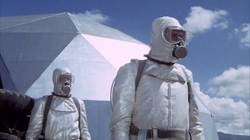 Movie still from “Phase IV” (1974), directed by Saul Bass – Two men in white suits and gas masks stand in front of an umbrella; Medium shot, Low angle