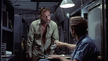 Movie still from “Phase IV” (1974), directed by Saul Bass – A man talking to another man in front of a table; Medium shot, Low angle