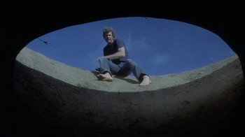 Movie still from “Phase IV” (1974), directed by Saul Bass – A man sitting on the side of a cement structure; Wide shot, Low angle