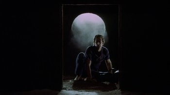 Movie still from “Phase IV” (1974), directed by Saul Bass – A man sitting on the ground in front of an open door; Wide shot, Low angle