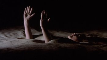 Movie still from “Phase IV” (1974), directed by Saul Bass – A person laying in the sand with their hands up; Wide shot, High angle