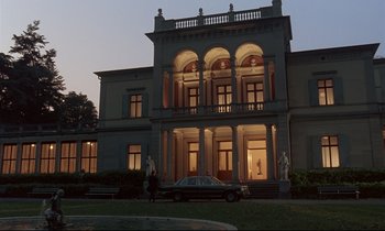 Movie still from “Phenomena” (1985), directed by Dario Argento – A car is parked in front of a large building; Extreme Wide shot, Low angle