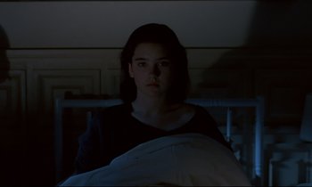 Movie still from “Phenomena” (1985), directed by Dario Argento – A woman in a dark room looking at the camera; Medium shot, High angle