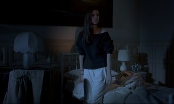 Movie still from “Phenomena” (1985), directed by Dario Argento – A woman standing in a dark room next to a bed; Medium shot, Low angle
