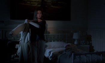 Movie still from “Phenomena” (1985), directed by Dario Argento – A woman standing in a dark room holding onto some clothes; Medium shot, Low angle