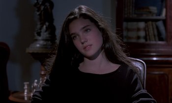 Movie still from “Phenomena” (1985), directed by Dario Argento – A young woman with long black hair sitting in front of a statue; Close Up shot, Over the shoulder angle