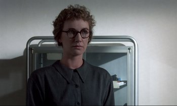Movie still from “Phenomena” (1985), directed by Dario Argento – A woman wearing glasses standing next to a bed; Close Up shot, Over the shoulder angle