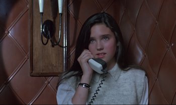 Movie still from “Phenomena” (1985), directed by Dario Argento – A woman sitting in a chair talking on a phone; Close Up shot, High angle