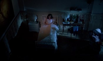 Movie still from “Phenomena” (1985), directed by Dario Argento – A woman sitting on top of a bed next to a table; Wide shot, High angle