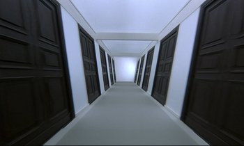 Movie still from “Phenomena” (1985), directed by Dario Argento – A long hallway with many black doors leading to a white room; Extreme Wide shot, Overhead angle