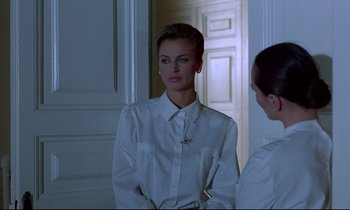 Movie still from “Phenomena” (1985), directed by Dario Argento – A woman in a white shirt looking at a mirror; Medium shot, Over the shoulder angle