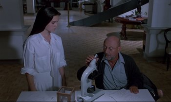 Movie still from “Phenomena” (1985), directed by Dario Argento – An older man and a young woman looking at a microscope; Medium shot, High angle
