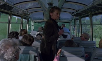 Movie still from “Phenomena” (1985), directed by Dario Argento – A woman standing on a bus with people sitting on the seats; Medium shot, Low angle