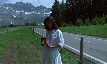 Movie still from “Phenomena” (1985), directed by Dario Argento – A woman standing in front of a road holding a box; Medium shot, Low angle