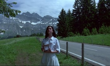 Movie still from “Phenomena” (1985), directed by Dario Argento – A woman standing in front of a road with mountains in the background; Medium shot, Low angle