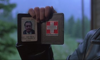 Movie still from “Phenomena” (1985), directed by Dario Argento – A person holding a first - aid kit with a picture of a man in front of it; Close Up shot, Overhead angle