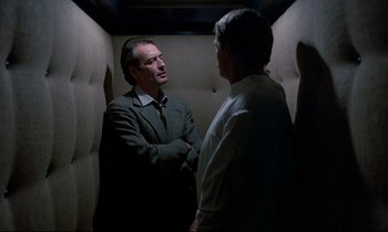 Movie still from “Phenomena” (1985), directed by Dario Argento – Two men are talking in a dark room; Medium shot, Low angle
