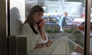 Movie still from “Phenomena” (1985), directed by Dario Argento – A woman sitting on a bench talking on a phone; Medium shot, Low angle