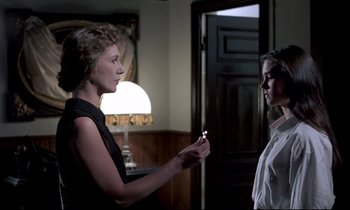 Movie still from “Phenomena” (1985), directed by Dario Argento – Two women are standing in a room and one is holding a cigarette; Medium shot, Over the shoulder angle