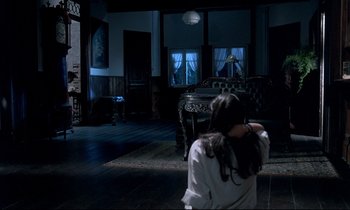 Movie still from “Phenomena” (1985), directed by Dario Argento – A woman standing in front of a chair in a dark room; Wide shot, High angle