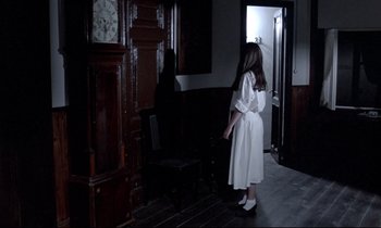 Movie still from “Phenomena” (1985), directed by Dario Argento – A woman in a white dress standing in front of a grandfather clock; Wide shot, High angle
