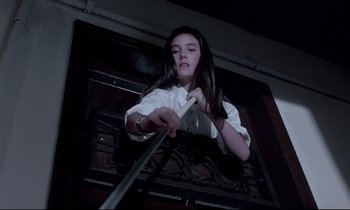 Movie still from “Phenomena” (1985), directed by Dario Argento – A woman in a white shirt is holding onto some wires; Medium shot, Overhead angle