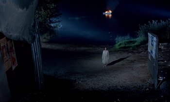 Movie still from “Phenomena” (1985), directed by Dario Argento – A woman standing in the dark in front of a burning tree; Extreme Wide shot, High angle