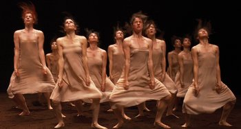 Movie still from “Pina” (2011), directed by Wim Wenders – A group of people in white dresses dancing on a stage; Wide shot, High angle