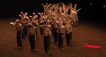 Movie still from “Pina” (2011), directed by Wim Wenders – A group of people standing on top of a dirt field; Extreme Wide shot, High angle