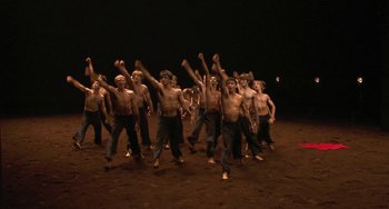 Movie still from “Pina” (2011), directed by Wim Wenders – A group of shirtless men are dancing on the ground; Extreme Wide shot, High angle