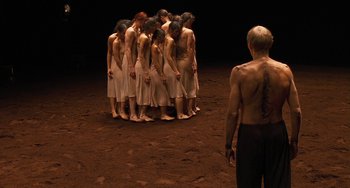 Movie still from “Pina” (2011), directed by Wim Wenders – A group of people standing in a circle on a dirt field; Wide shot, High angle