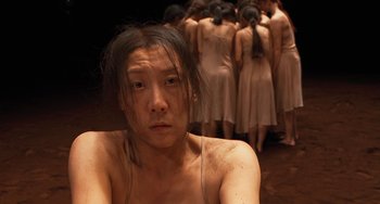 Movie still from “Pina” (2011), directed by Wim Wenders – A man with long black hair sitting in front of a group of women; Close Up shot, High angle