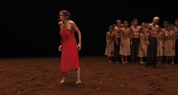 Movie still from “Pina” (2011), directed by Wim Wenders – A woman in a red dress standing in front of a group of people; Wide shot, High angle