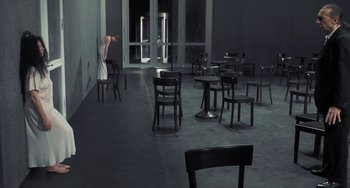Movie still from “Pina” (2011), directed by Wim Wenders – A person standing in front of some chairs in an empty room; Wide shot, Over the shoulder angle