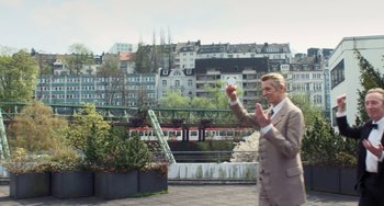 Movie still from “Pina” (2011), directed by Wim Wenders – A man in a brown suit holding up his hand; Wide shot, Low angle