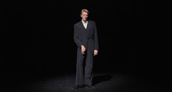 Movie still from “Pina” (2011), directed by Wim Wenders – A man wearing a suit and tie standing on a stage; Medium shot, Low angle