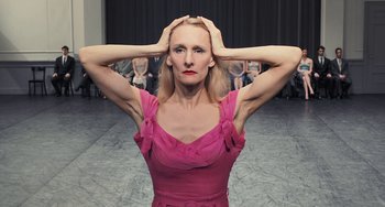 Movie still from “Pina” (2011), directed by Wim Wenders – A woman in a pink dress holding her hands to her head; Close Up shot, Low angle