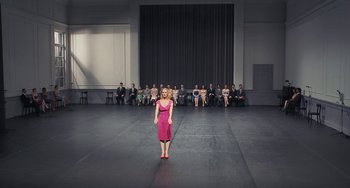 Movie still from “Pina” (2011), directed by Wim Wenders – A woman standing in front of a group of people in a room; Extreme Wide shot, High angle