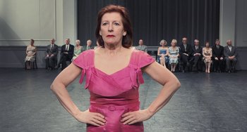 Movie still from “Pina” (2011), directed by Wim Wenders – A woman in a pink dress standing in front of a group of people; Medium shot, Low angle