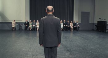 Movie still from “Pina” (2011), directed by Wim Wenders – A man in a black suit standing in front of a group of people; Wide shot, High angle