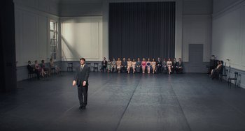 Movie still from “Pina” (2011), directed by Wim Wenders – A group of people sitting in a room with a man standing in front of them; Wide shot, High angle