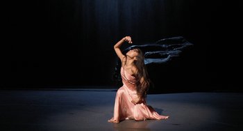 Movie still from “Pina” (2011), directed by Wim Wenders – A woman in a pink dress on a stage; Wide shot, Low angle