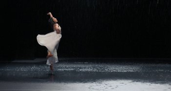 Movie still from “Pina” (2011), directed by Wim Wenders – A woman in a white dress is dancing in the rain; Wide shot, Low angle