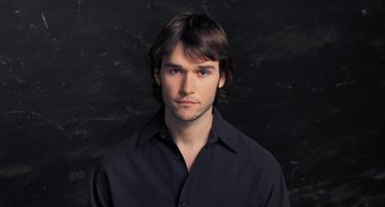 Movie still from “Pina” (2011), directed by Wim Wenders – A man with long brown hair wearing a black shirt; Close Up shot, Low angle