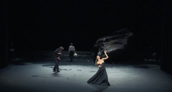 Movie still from “Pina” (2011), directed by Wim Wenders – A woman in a black dress is standing in the middle of a stage; Extreme Wide shot, High angle
