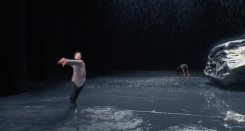 Movie still from “Pina” (2011), directed by Wim Wenders – A man is standing in the rain with his arms outstretched; Extreme Wide shot, High angle