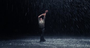 Movie still from “Pina” (2011), directed by Wim Wenders – A man standing in the middle of a rain storm holding his hands up; Wide shot, Low angle