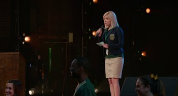 Movie still from “Pitch Perfect 2” (2015), directed by Elizabeth Banks – A woman standing on a stage holding a microphone; Medium shot, Over the shoulder angle